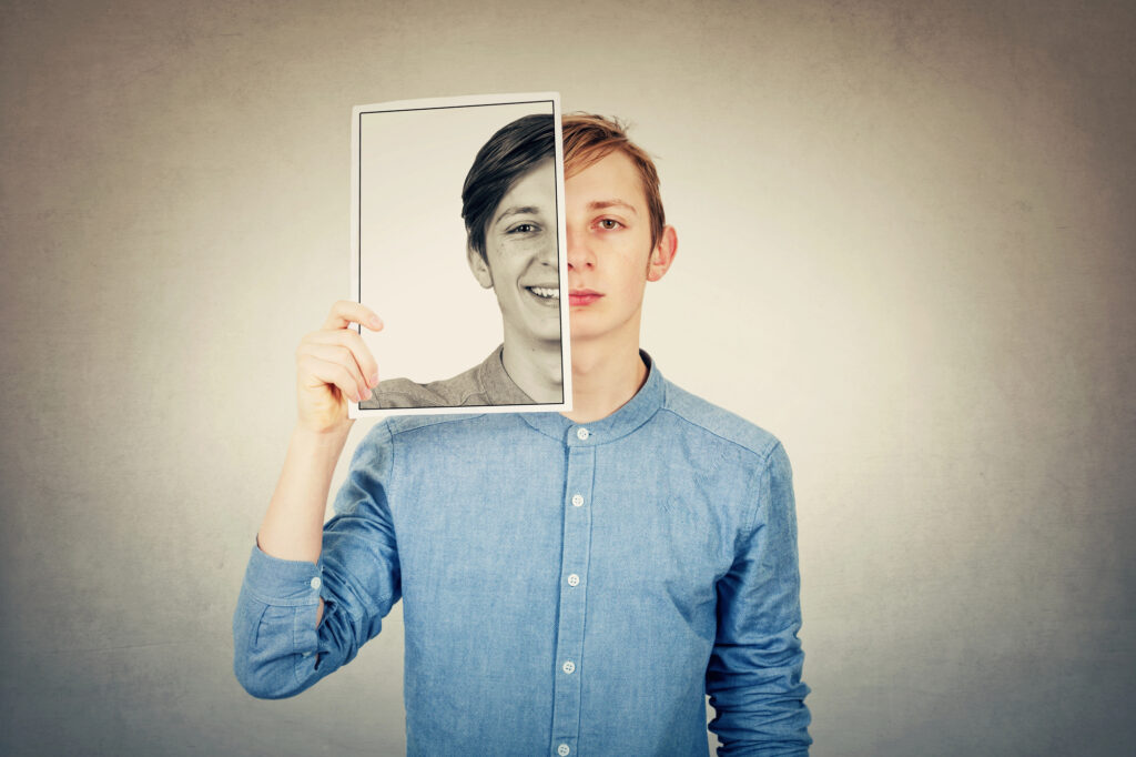 Person holding a picture of a smiling face over their own sad expression