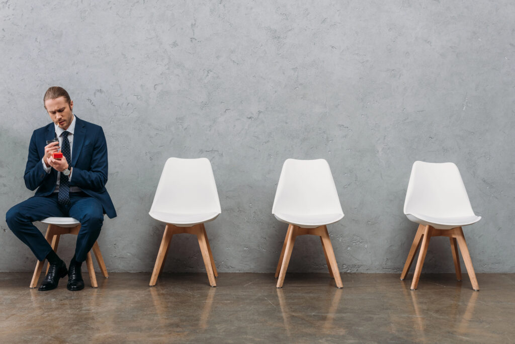 Man sitting alone in a waiting room holding a cup, with empty chairs beside him.