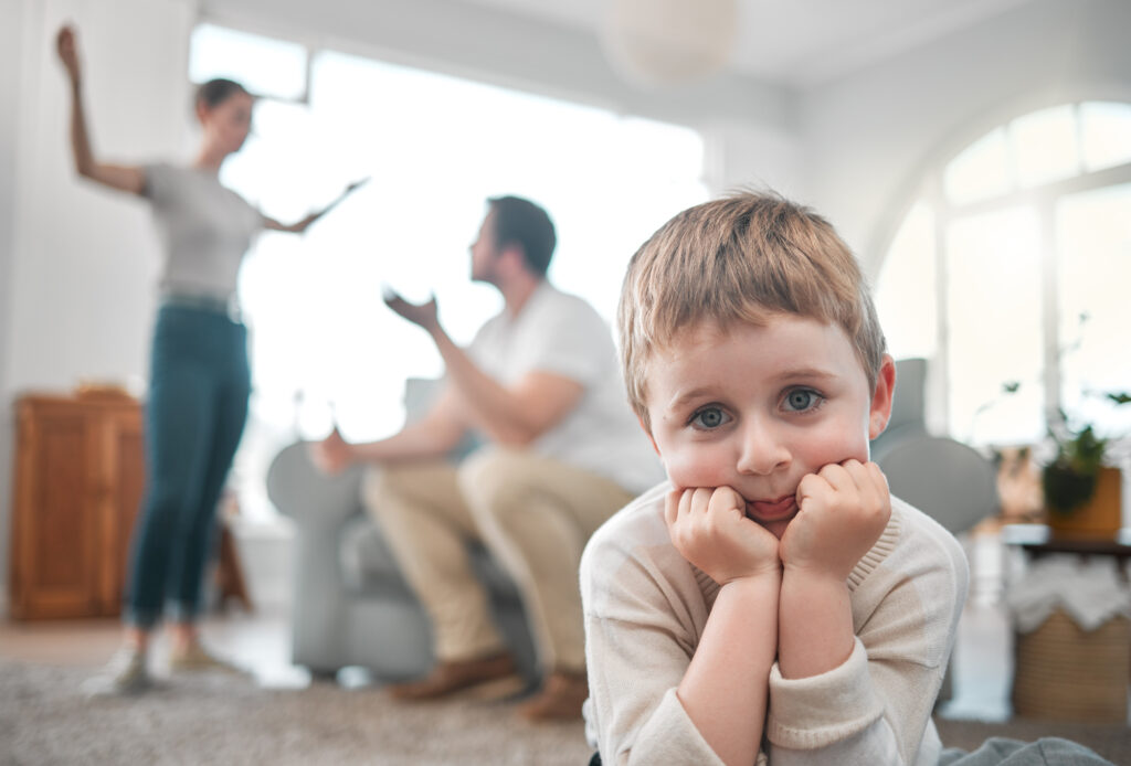 Young boy sitting sadly in the foreground while a couple argues in the background