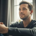 A calm man sitting in gentle morning light, hands clasped, symbolizing healing self-worth and inner peace after years of self-criticism.